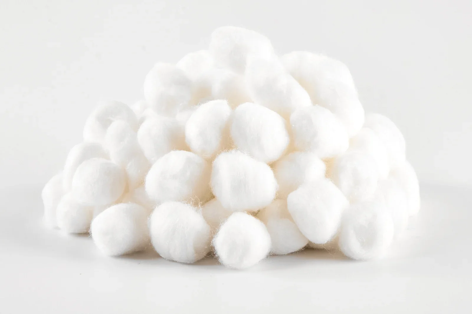 A pile of white absorbent cotton balls on a light grey studio background