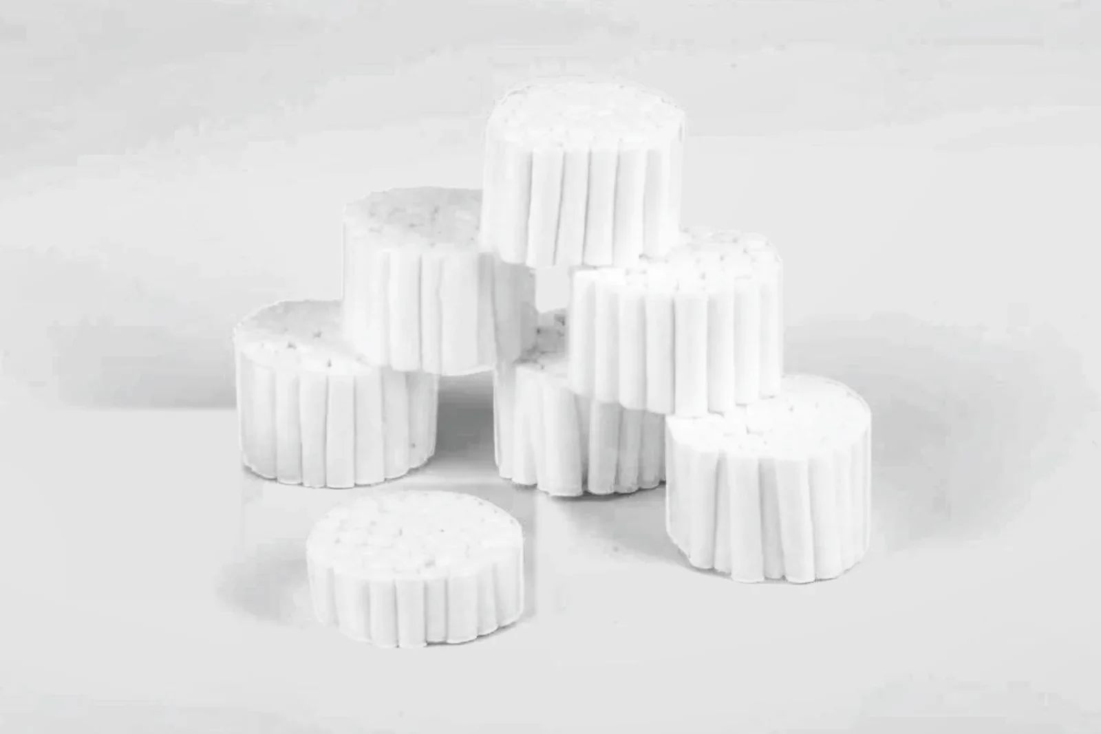 Bundles of white dental cotton rolls stacked on a light grey studio background